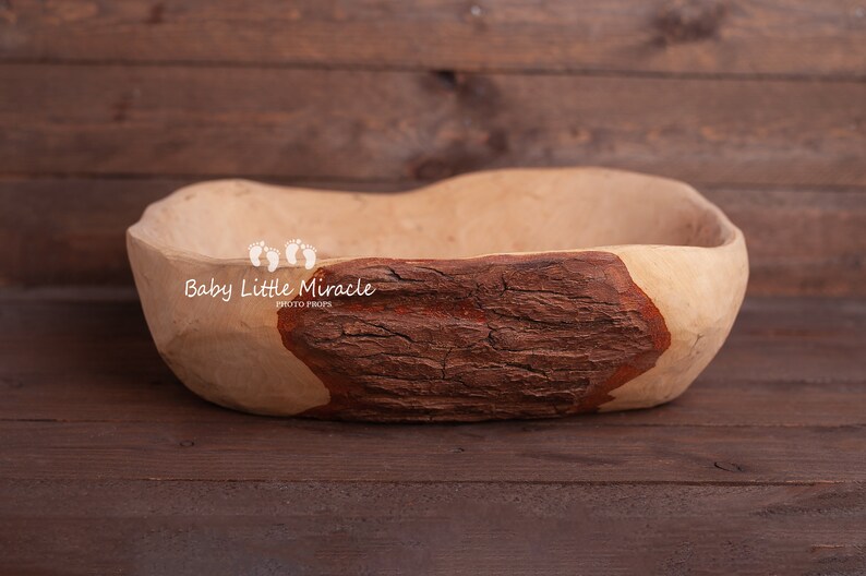 May include: A large, wooden bowl with a natural brown finish. The bowl has a rough, textured surface and a dark brown patch on one side. The bowl is ideal for newborn photography props.