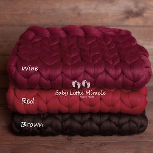 May include: Three braided chunky knit blankets in wine, red, and brown colors. The blankets are stacked on top of each other. The text "Baby Little Miracle Photo Props" is printed on the red blanket.