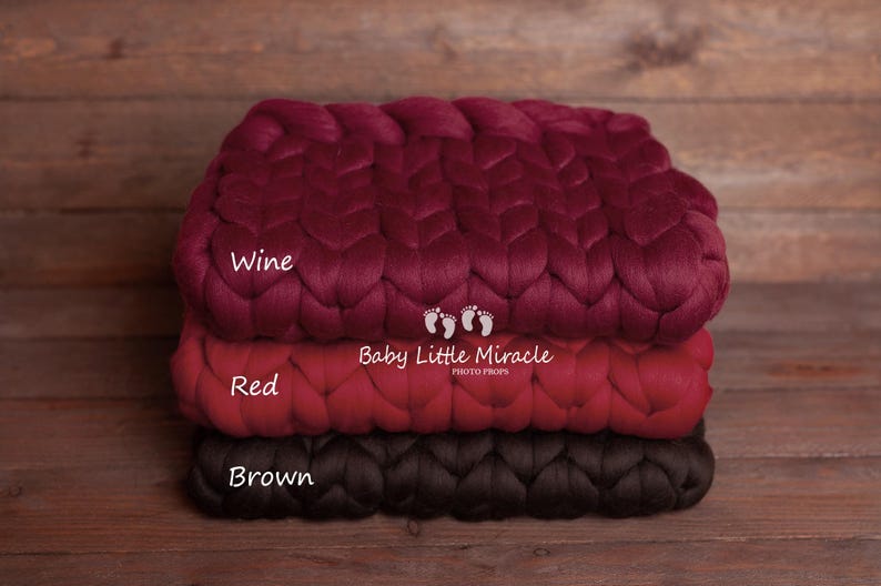 May include: Three braided chunky knit blankets in wine, red, and brown colors. The blankets are stacked on top of each other. The text "Baby Little Miracle Photo Props" is printed on the red blanket.