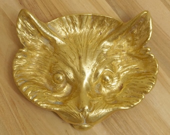 Puede incluir: Una escultura de cabeza de zorro de metal dorado. La escultura está detallada con pelo y tiene una expresión realista.