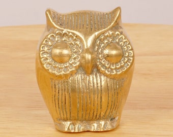 May include: A gold-colored brass owl figurine with detailed eyes and a textured body.