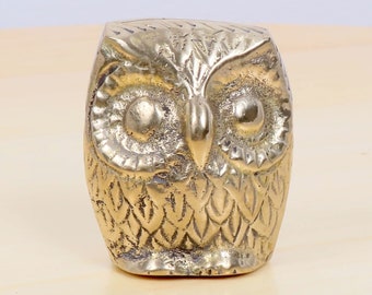 May include: A gold-colored metal owl figurine with detailed features, including eyes, beak, and feathers.