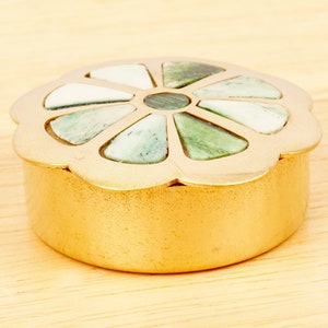 Puede incluir: Una caja de metal dorado con un diseño de flor. La flor está hecha de piedra verde y blanca.