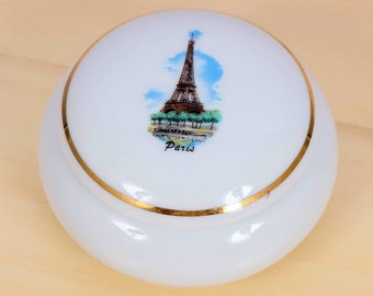Könnte beinhalten: Weiße Keramik-Schmuckdose mit goldfarbenem Rand und einem gemalten Bild des Eiffelturms in Paris, Frankreich.