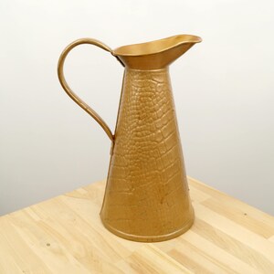 May include: A gold metal pitcher with a textured, crocodile-skin-like design. The pitcher has a wide mouth and a handle.