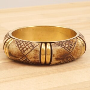 Könnte beinhalten: Ein braunes und goldenes Armreif-Armband mit geometrischem Muster. Das Armband ist aus Holz und Metall.