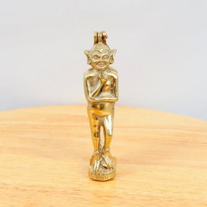 May include: A vintage brass nutcracker in the shape of a pixie or elf. The figure has a smiling face, pointed ears, and is standing on a base with text. The nutcracker is a golden color and has a hinged mechanism at the top.