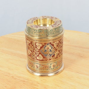 May include: A brass ashtray with a floral design in red, green, and gold. The ashtray has a round shape and a raised rim.