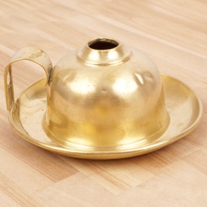 May include: A gold-colored brass oil lamp with a round, domed top and a handle. The lamp sits on a matching saucer.