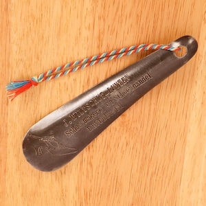 May include: A metal shoe last with a red, white, and blue ribbon attached. The last has the text "J. WitsCHUT-LUTTEN Schoenmakerij en schoenenhandel REYTHUISEN" engraved on it.