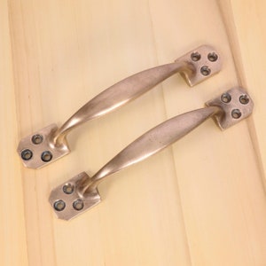 May include: Two antique brass door handles with a curved design and four screw holes on each handle.