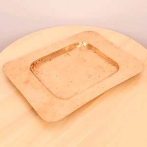 May include: A square, hammered copper serving tray with a raised rim. The tray has a slightly distressed finish and is ideal for serving snacks or appetizers.