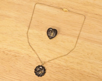Op de afbeelding: Een gouden ketting met een zwarte en gouden hanger met een Japans tafereel. Een bijpassende hartvormige broche met een vergelijkbaar ontwerp is ook inbegrepen.