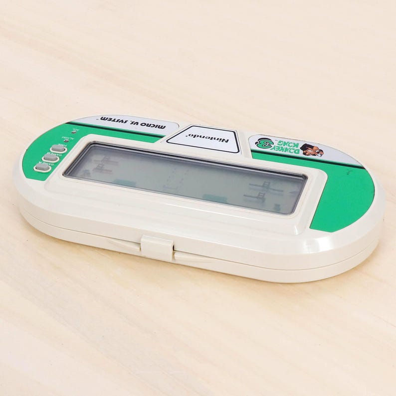 May include: A vintage Nintendo Micro Vs. System handheld game console featuring the Donkey Kong game. The console has a white body with green accents and a small LCD screen. The game's title and Nintendo logo are visible.