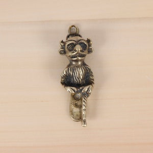 Peut inclure: Un crochet en laiton en forme de petite créature poilue avec des cornes et un bâton dans la main. Le crochet est monté sur une surface en bois.