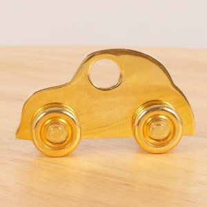 May include: A gold-colored metal car figurine with a hole in the roof. The car has a rounded shape and two large wheels.