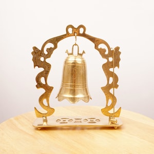 May include: A gold-colored metal bell with intricate dragon designs on the stand. The bell hangs from a hook on the stand.
