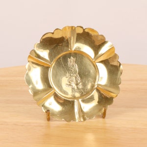 Könnte beinhalten: Eine goldfarbene Metallschale mit einem gewellten Rand. Die Schale hat ein erhabenes Design einer Figur, die auf einem Pilz sitzt, mit dem Text "Cornish Pixie" darunter.