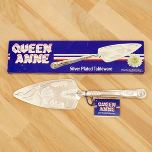 May include: Silver plated cake server with an ornate design. The server is in a blue box with the words "Queen Anne Silver Plated Tableware" printed on it.