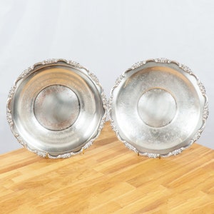 May include: Two silver serving dishes with ornate edges, sitting on a wooden surface.
