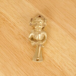 Peut inclure: Un heurtoir de porte en forme de singe doré avec un design détaillé. Le singe est assis, les jambes croisées, et tient un bâton dans ses mains.
