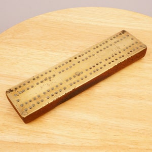May include: A vintage brass cribbage board with a wooden frame. The board has a worn, antique look and is ready for a game.