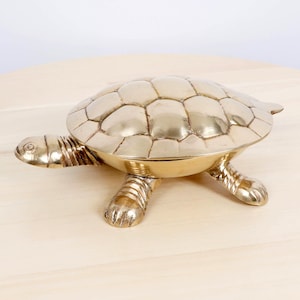 Könnte beinhalten: Eine Messing-Schildkrötenfigur mit detailliertem Panzer, Kopf und Beinen. Die Schildkröte ist ein dekorativer Gegenstand, wahrscheinlich eine Schmuckschatulle oder eine kleine Skulptur. Das Messing hat eine polierte, reflektierende Oberfläche.
