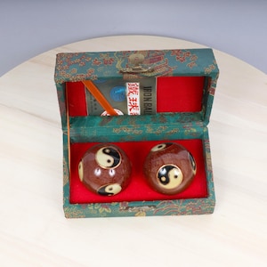 May include: Two brown and black yin yang balls in a green and gold box with red lining. The box has a label that says "Iron Balls" in English and Chinese characters.
