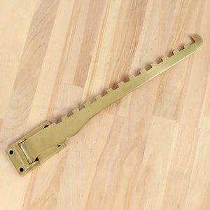 Puede incluir: Un gancho de pared decorativo de metal, de color latón, con un borde festoneado. El gancho está diseñado para sujetar un abrigo, un sombrero u otros objetos.