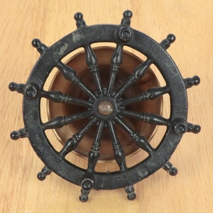 May include: Black metal ship's wheel with a brass center and spokes. The wheel has a decorative design and is a nautical themed item.