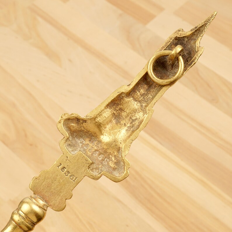 Peut inclure: Outil de chemin&eacute;e en m&eacute;tal dor&eacute; avec un motif d&eacute;coratif repr&eacute;sentant un b&acirc;timent. L'outil a un anneau sur le dessus et le num&eacute;ro "16861" est grav&eacute; sur le c&ocirc;t&eacute;.