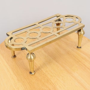 May include: A brass pot stand with a decorative design and four legs. The stand is made of a shiny, gold-coloured metal.