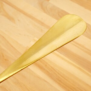 Peut inclure: Un chausse-pied en or avec une surface lisse l&eacute;g&egrave;rement incurv&eacute;e.