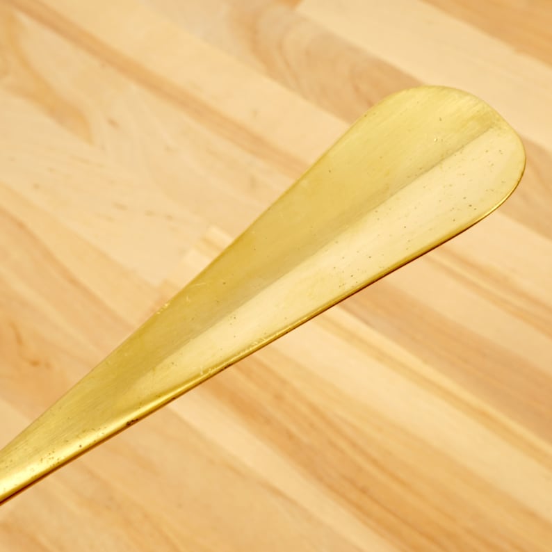 Peut inclure: Un chausse-pied en or avec une surface lisse l&eacute;g&egrave;rement incurv&eacute;e.