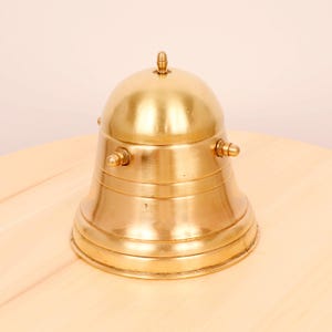 May include: A gold-toned bell-shaped desk accessory with a domed top and a smooth, polished finish.