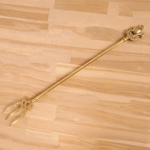 Puede incluir: Una herramienta de chimenea dorada con un mango decorativo y un extremo de tres puntas.