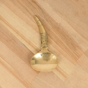 May include: A gold-colored metal spoon with a decorative handle and a round bowl. The bowl of the spoon has the word "YORK" engraved on it.