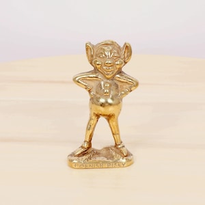 Peut inclure: Une figurine en laiton de couleur dorée représentant un lutin de Cornouailles avec un sourire malicieux, debout les mains sur les hanches. La base de la figurine est inscrite "Cornish Pixie".