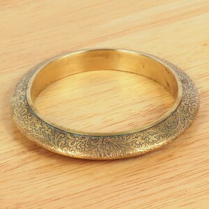 Könnte beinhalten: Ein goldfarbenes Armreif-Armband mit einem komplizierten, in die Oberfläche geätzten Blumenmuster.