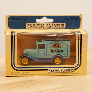 May include: A blue and yellow toy delivery truck with a white roof and a "Tucher" logo on the side. The truck is in a box with the words "Days Gone" on it.