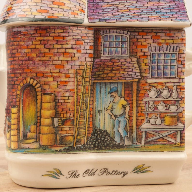 K&ouml;nnte beinhalten: Eine Keramik-Teekanne in Form eines Backsteingeb&auml;udes mit einer braunen Backsteinfassade, einer blauen T&uuml;r und einem Schild mit der Aufschrift "The Old Pottery". Das Geb&auml;ude hat zwei Fenster, eines mit Blick auf einen Mann in einem blauen Hemd und einer blauen M&uuml;tze, und das andere mit Blick auf ein Regal mit Teekannen.