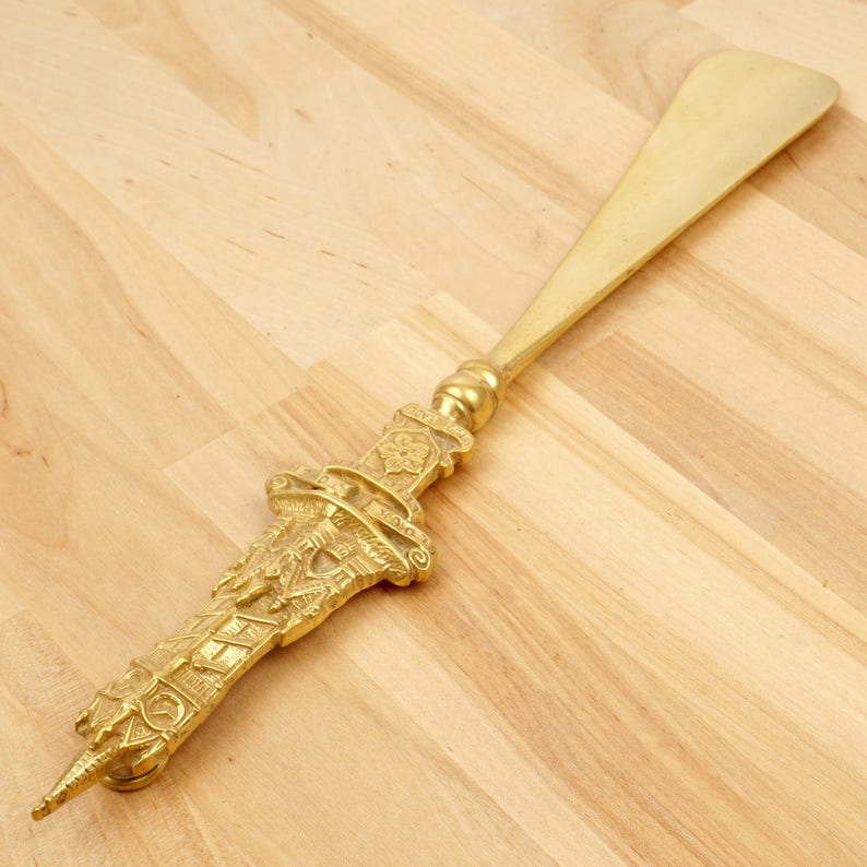 Peut inclure: Un chausse-pied en or avec un design orn&eacute; et d&eacute;taill&eacute;. Le manche est en forme de tour avec des sculptures complexes.