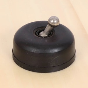 May include: A vintage-style, black light switch with a rounded base and a silver toggle. The switch has a circular design and is likely made of a durable material. The toggle is a small, silver ball on a metal arm.