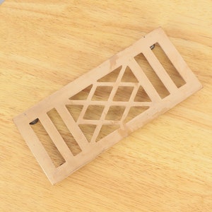May include: A brass vent cover with a geometric design. The cover has a diamond pattern with a triangle in the center.
