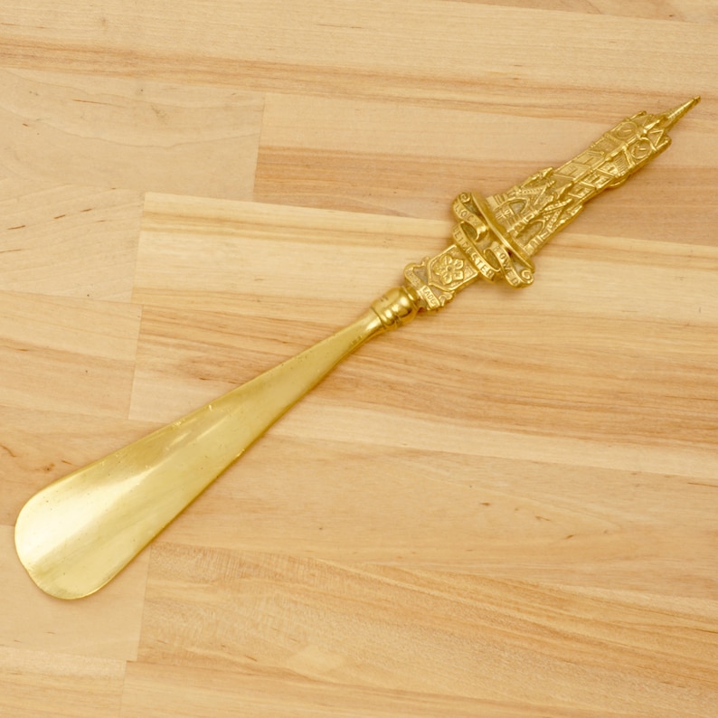 Peut inclure: Un chausse-pied en or avec une poign&eacute;e orn&eacute;e et d&eacute;taill&eacute;e. La poign&eacute;e est en forme de tour avec des sculptures complexes.