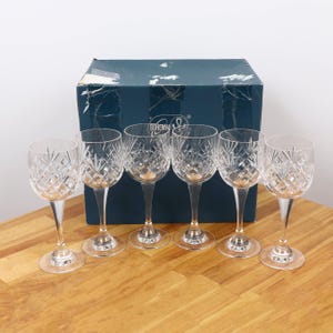 Peut inclure: Ensemble de six verres à vin en cristal transparent avec des motifs taillés en diamant. Les verres ont de longues tiges et des bases rondes. Une boîte bleu foncé avec le mot "Bohemia" est en arrière-plan.