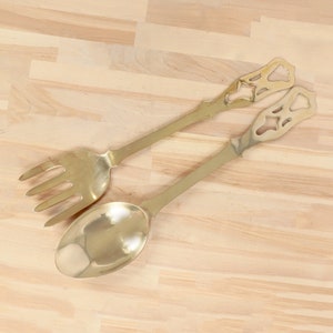 May include: A gold-toned metal serving set with a fork and a spoon. The handles have a decorative cutout design.