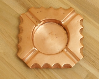 May include: A copper ashtray with a scalloped edge and four compartments. The ashtray is made of a shiny, polished copper.