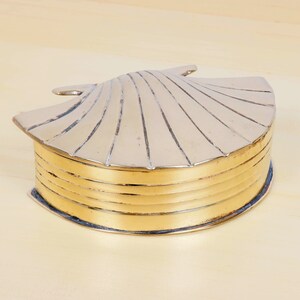 May include: A gold-colored brass trinket box shaped like a seashell. The box has a hinged lid with a ribbed design and a smooth, rounded bottom.