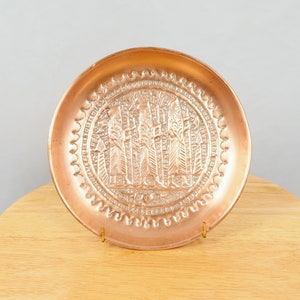 May include: A copper plate with an embossed design of four figures standing in front of a tree. The plate has a decorative border.
